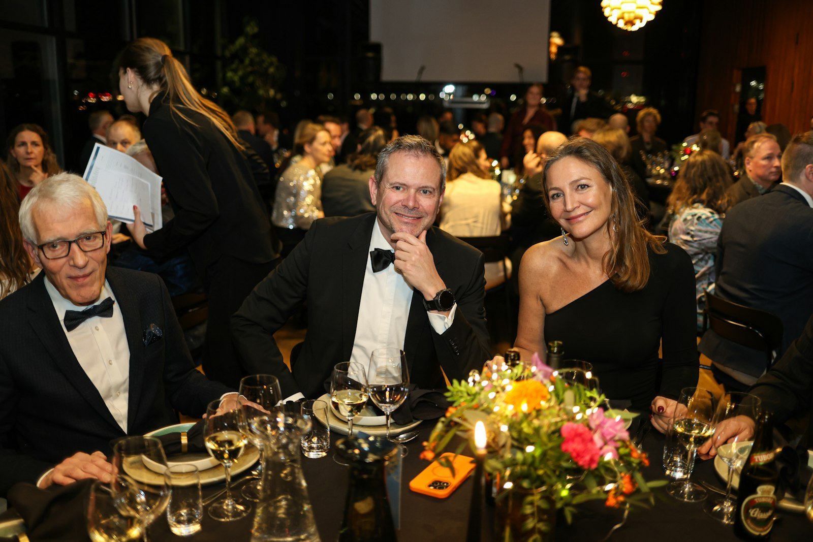 Cena de gala: tres personas conversan sentadas a la mesa de un evento formal.